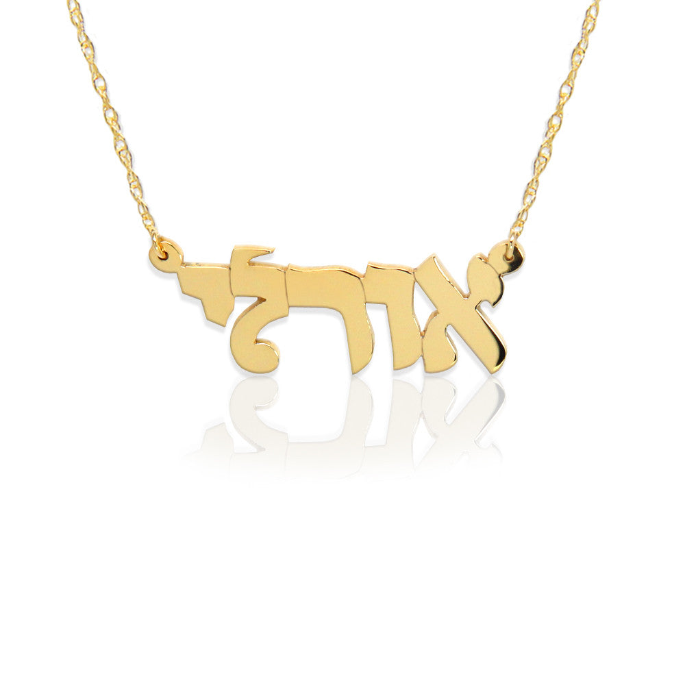 A gold Hebrew nameplate necklace on a delicate gold chain, displayed against a clean white background with a soft reflection underneath.
